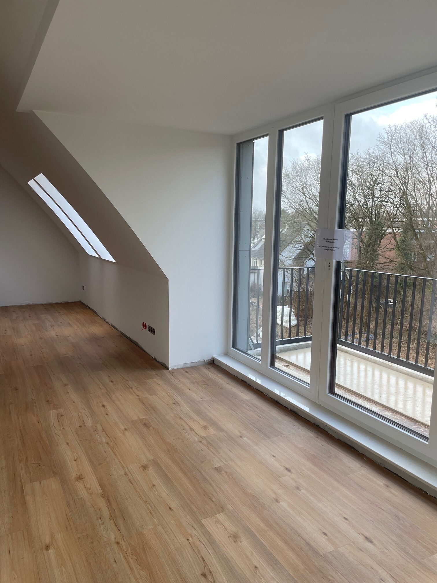 Geräumiges Zimmer mit großen Fenstern, Holzboden und Blick auf Bäume.