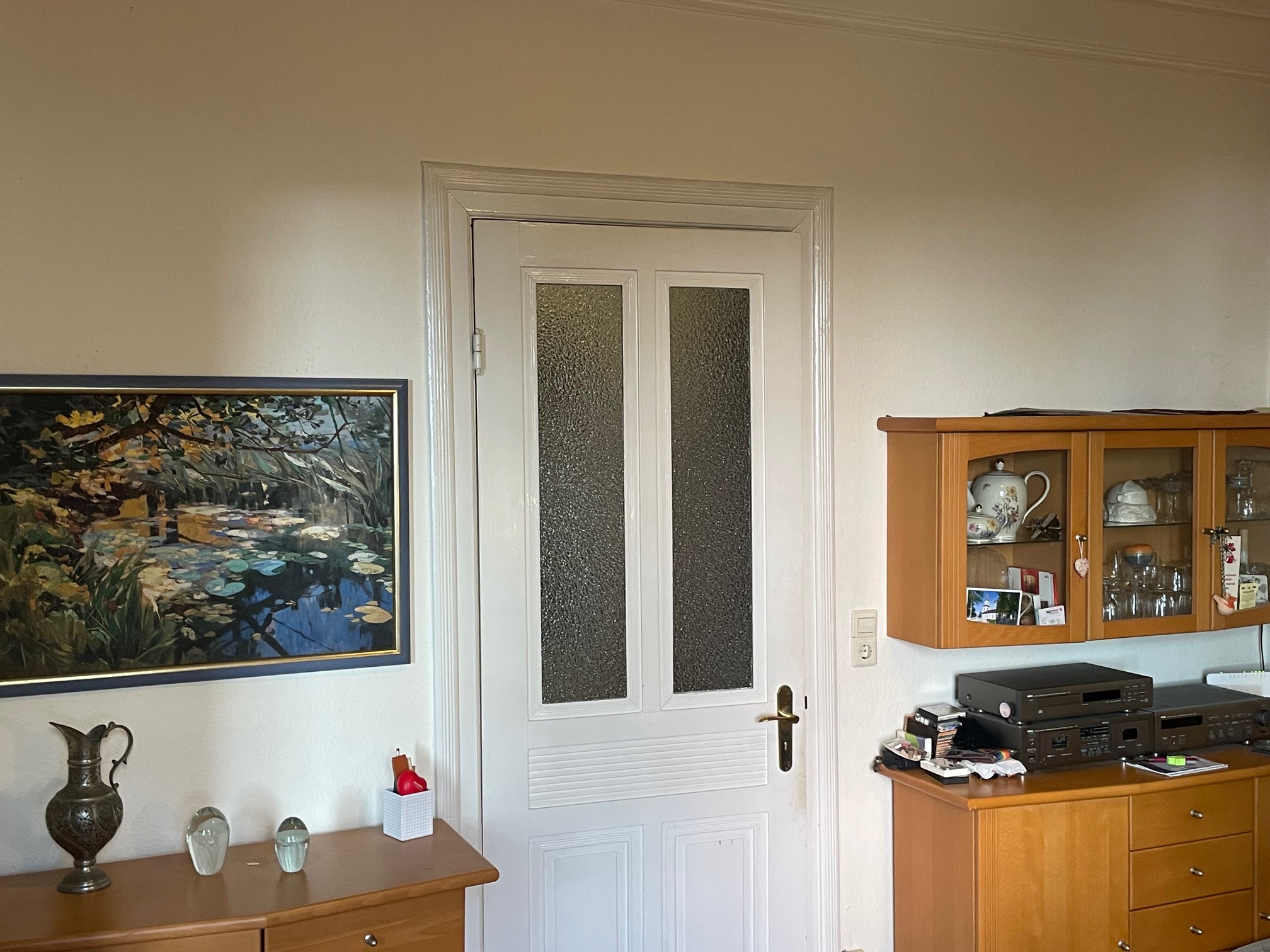 Tür in einem Wohnzimmer, mit Holzschrank, Gemälde, Vasen und Technik-Geräten, warmes Licht.